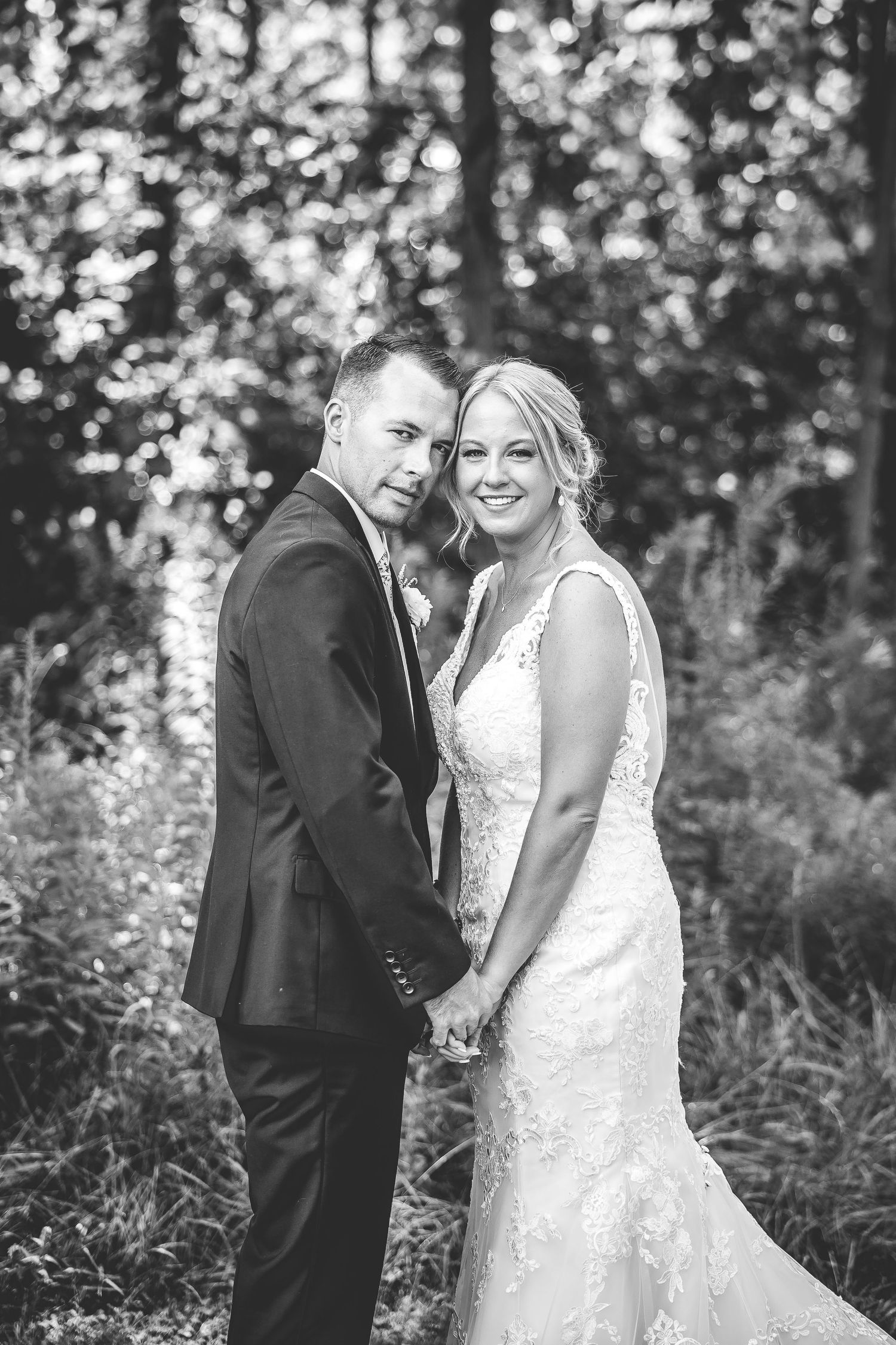 A black and white wedding portrait capturing a tender moment between newlyweds in a forest setting.