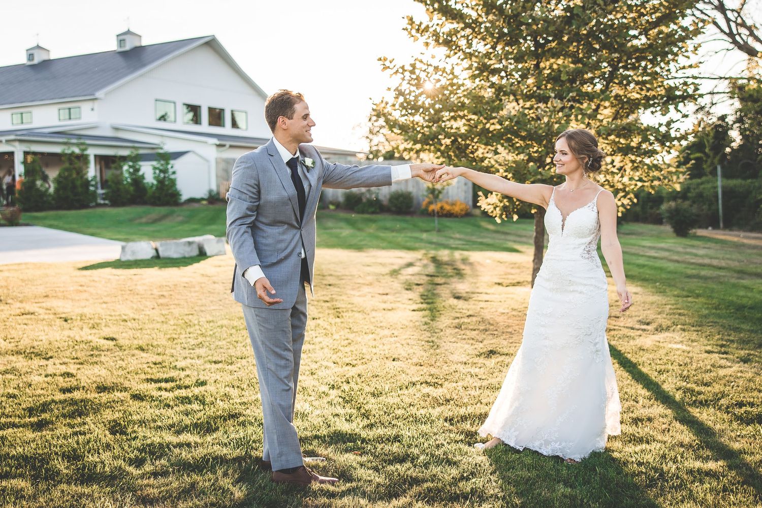 A couple in wedding attire shares a playful moment on a sun-drenched lawn.