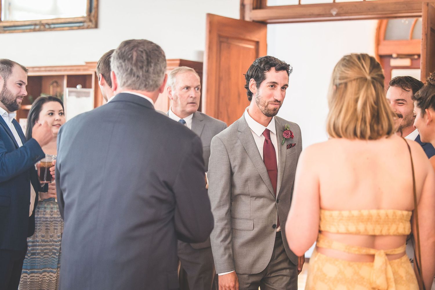 Wedding guests mingling in an elegant indoor venue with wooden trim and natural lighting.