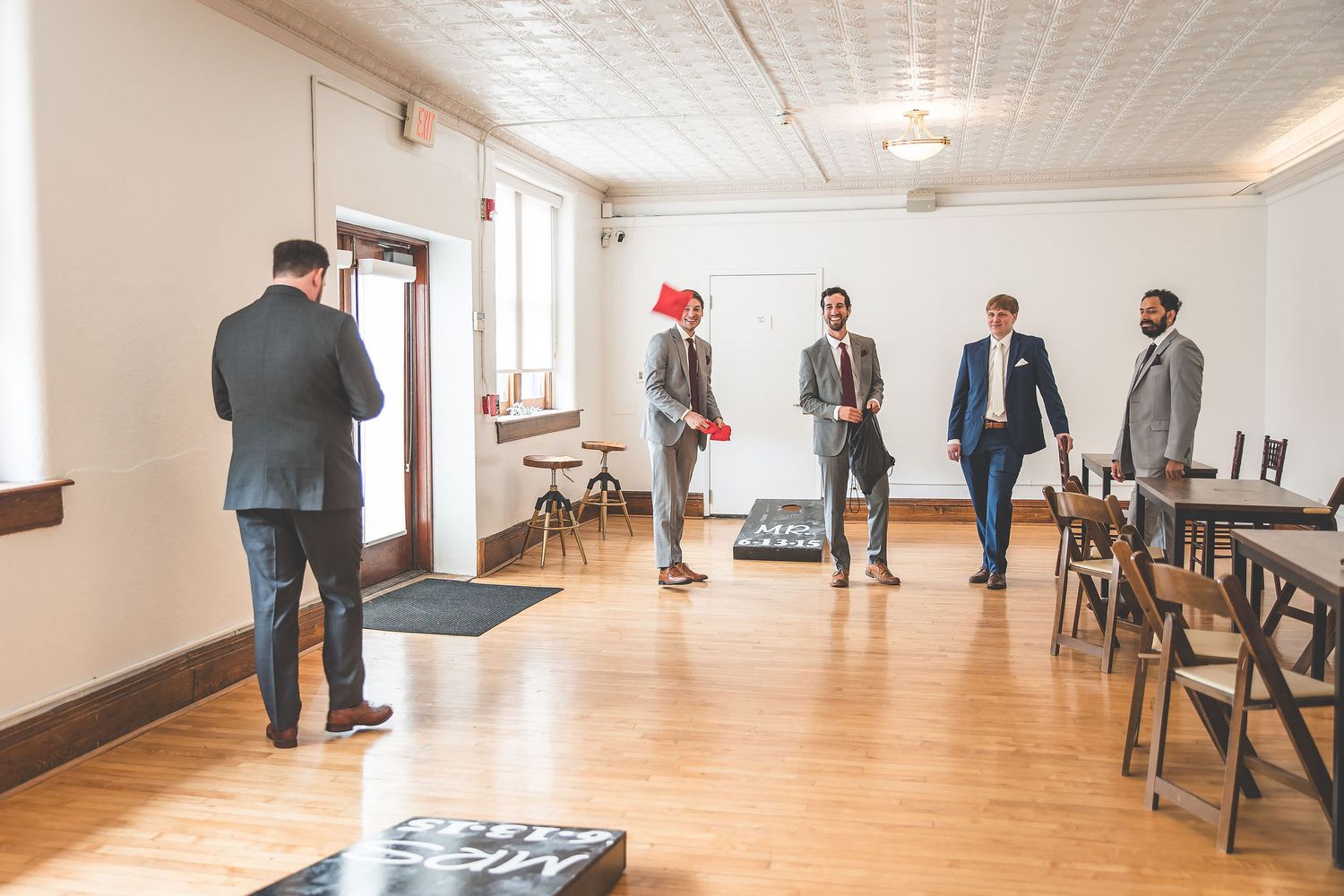 Groomsmen socializing in formal suits in a bright indoor venue space.