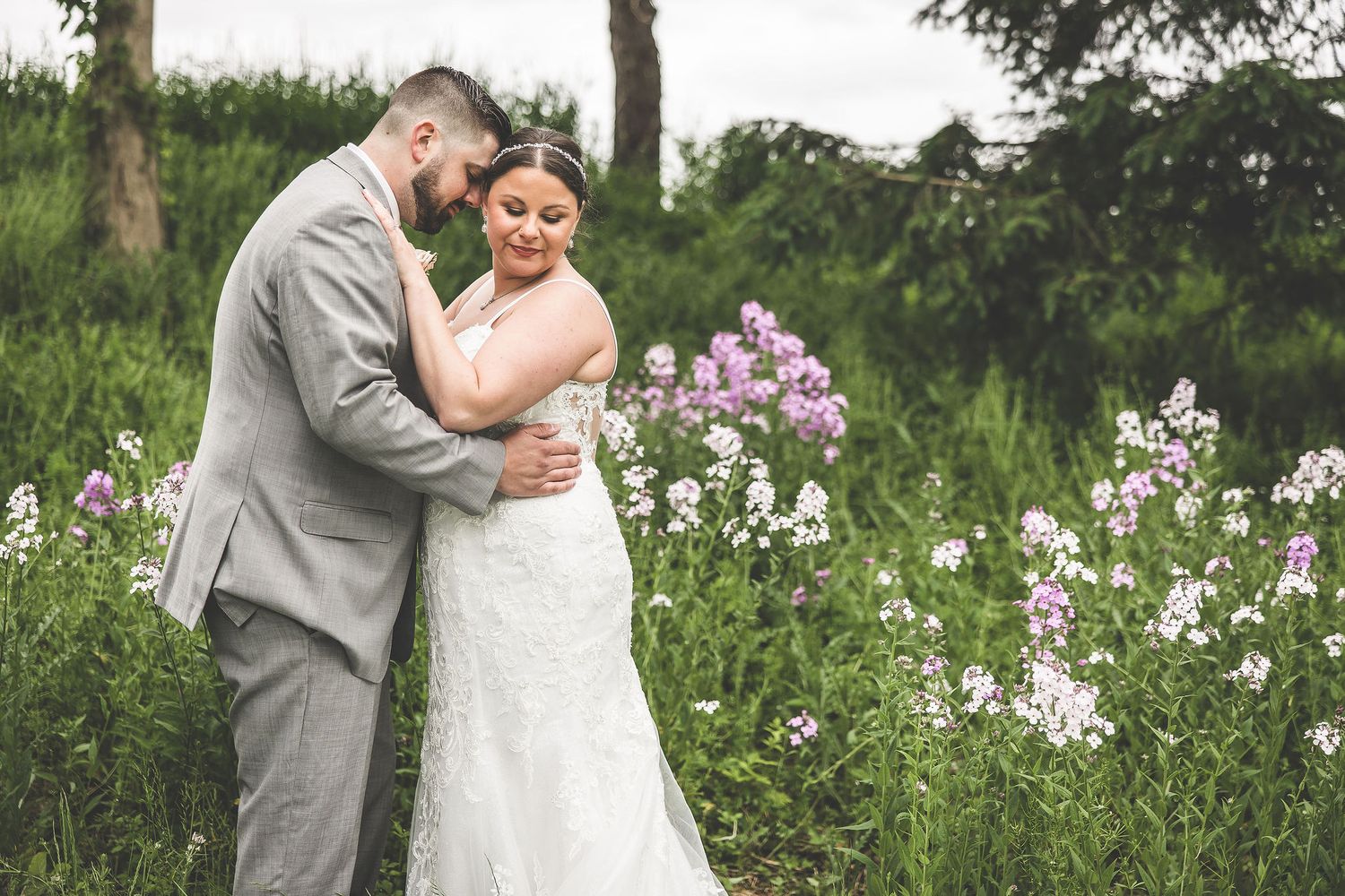 A tender moment between newlyweds surrounded by blooming wildflowers and tall trees.