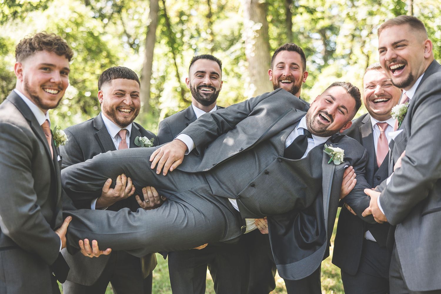 Wedding party men share playful candid moments in grey suits during outdoor photo session.