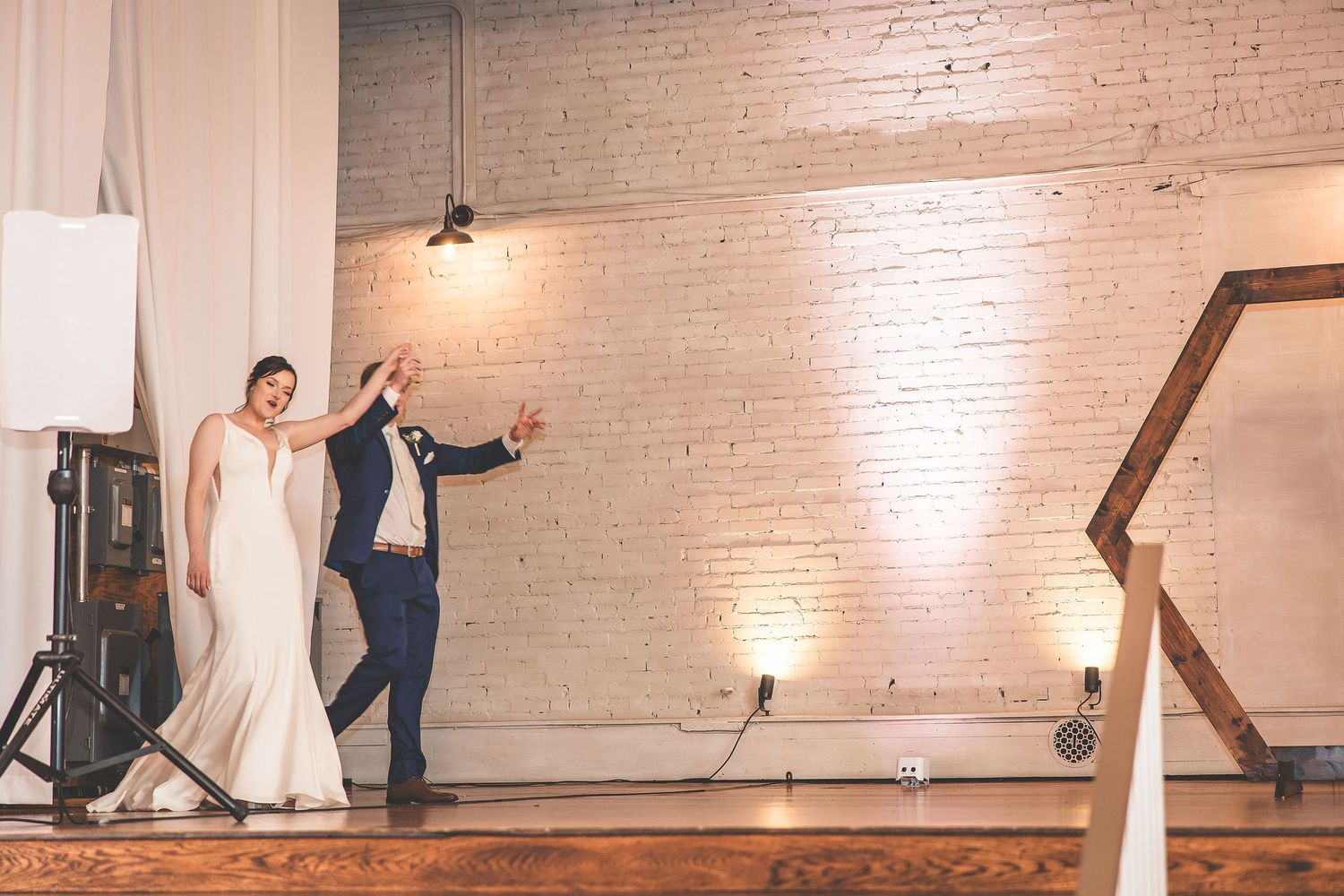 Couple dancing in an elegant venue with white brick walls and ambient lighting.