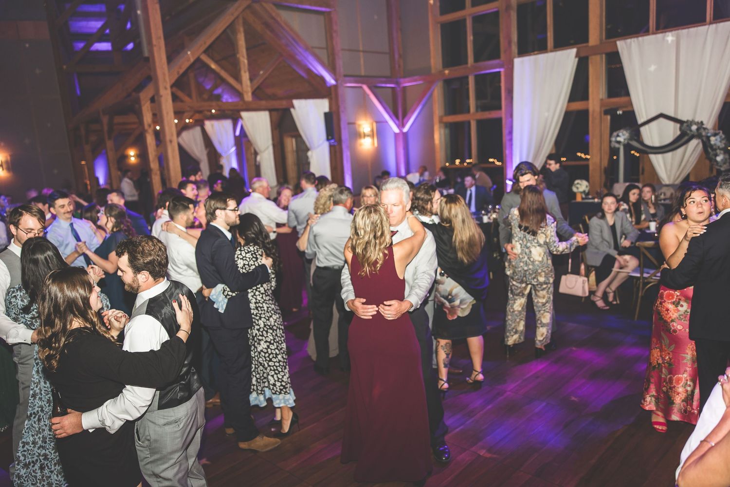 Wide shot of wedding reception venue with purple uplighting and guests dancing on the floor.