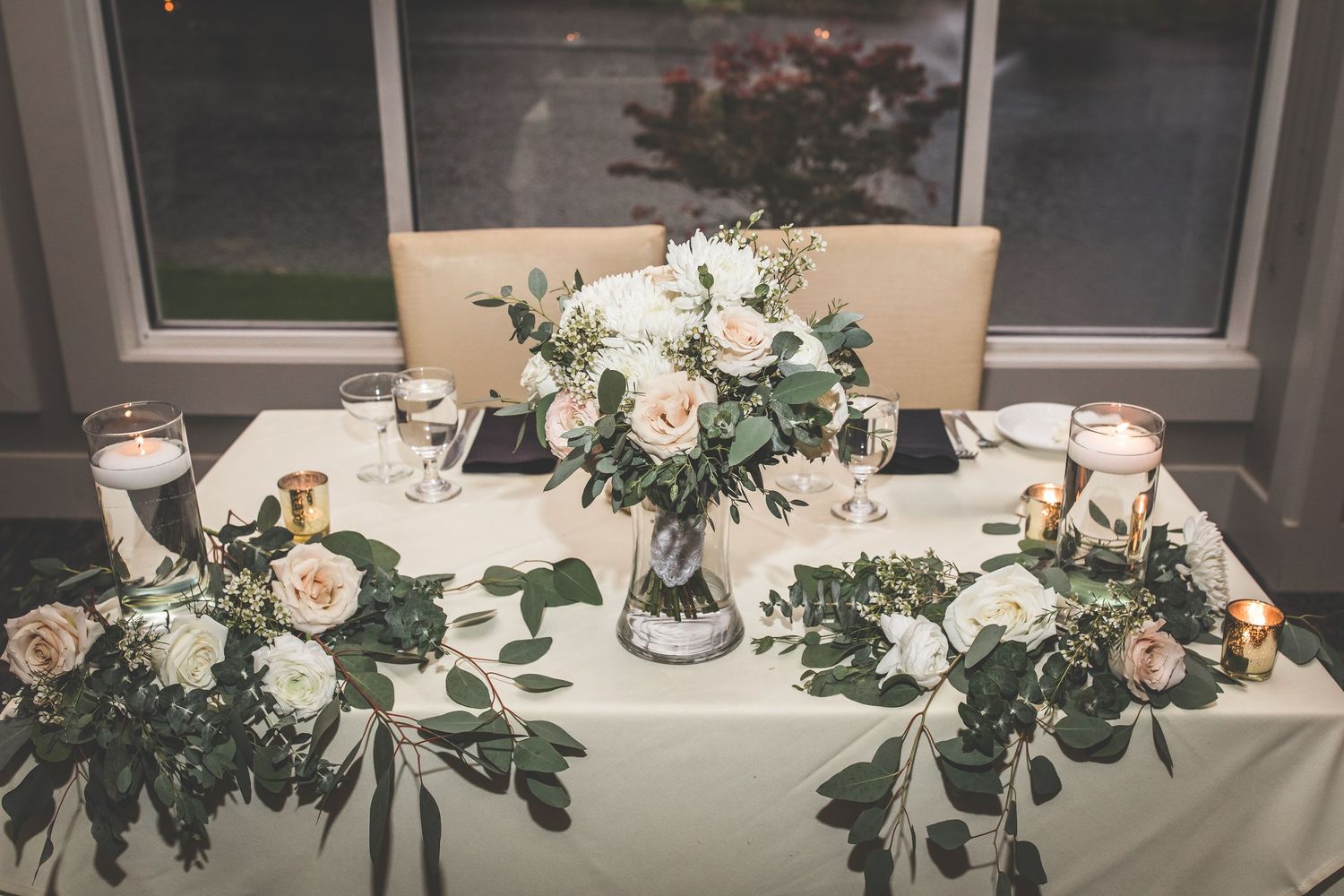 Elegant wedding reception table decorated with white floral arrangements and greenery.