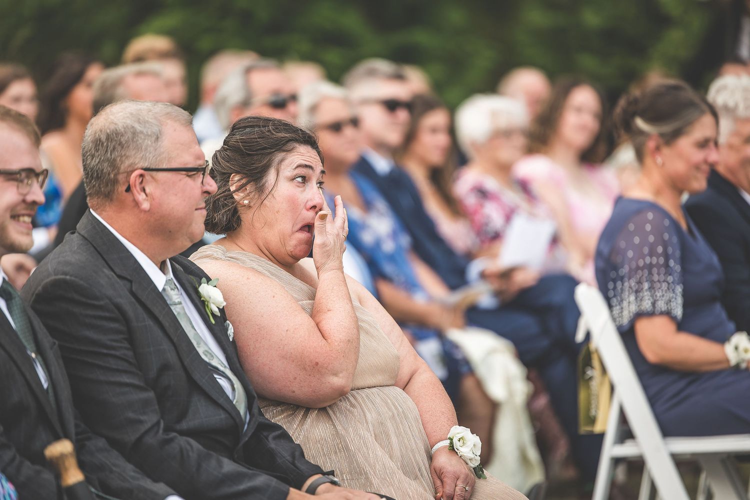 Wedding guests show emotional reactions while seated during outdoor ceremony.