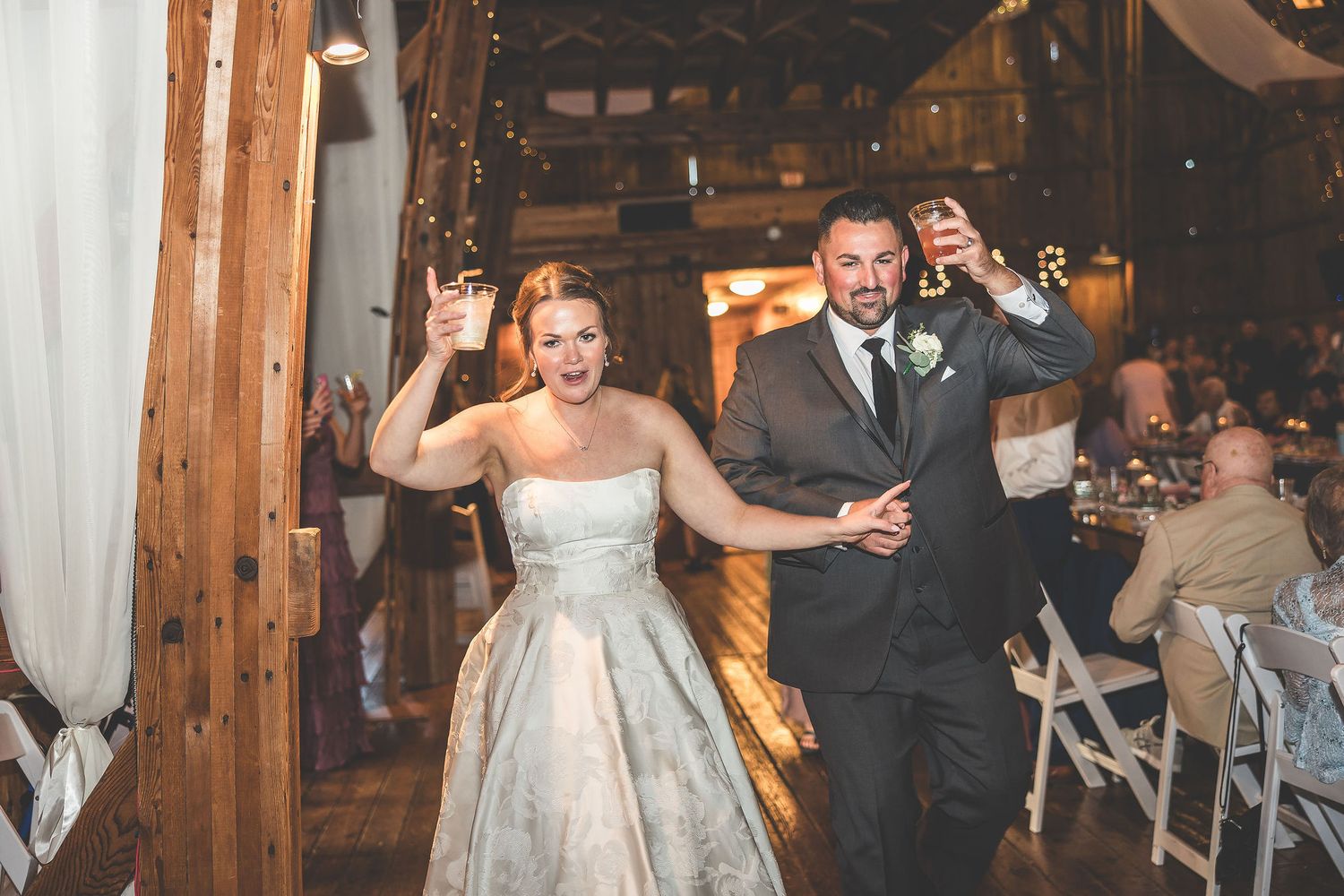 Wedding reception moments in a rustic barn venue with wooden walls and white draping.