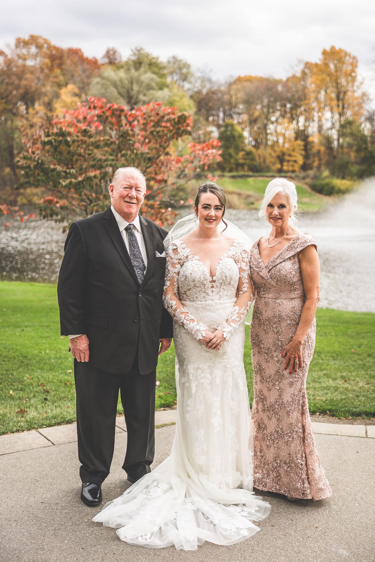 Autumn outdoor wedding photos by a lake with fall foliage in the background.