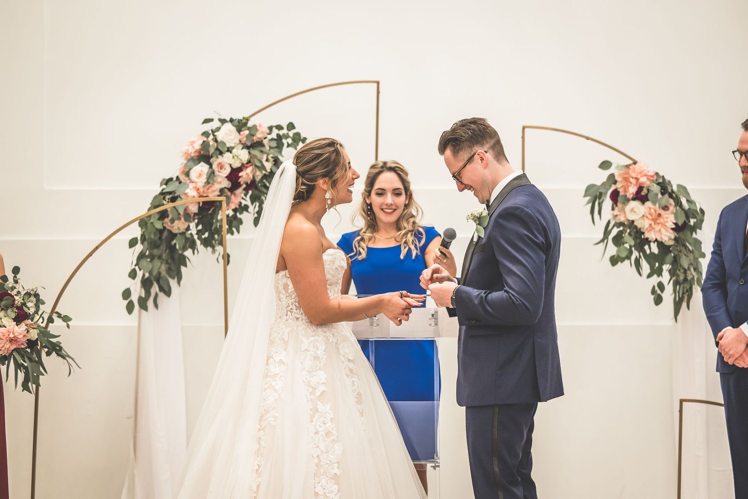 Wedding ceremony moments under copper arch with blue-dressed officiant.
