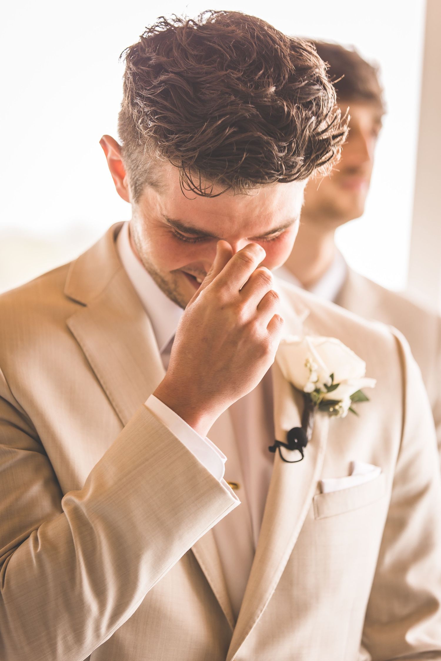 Candid emotional moment of groomsman wiping tears during wedding ceremony.