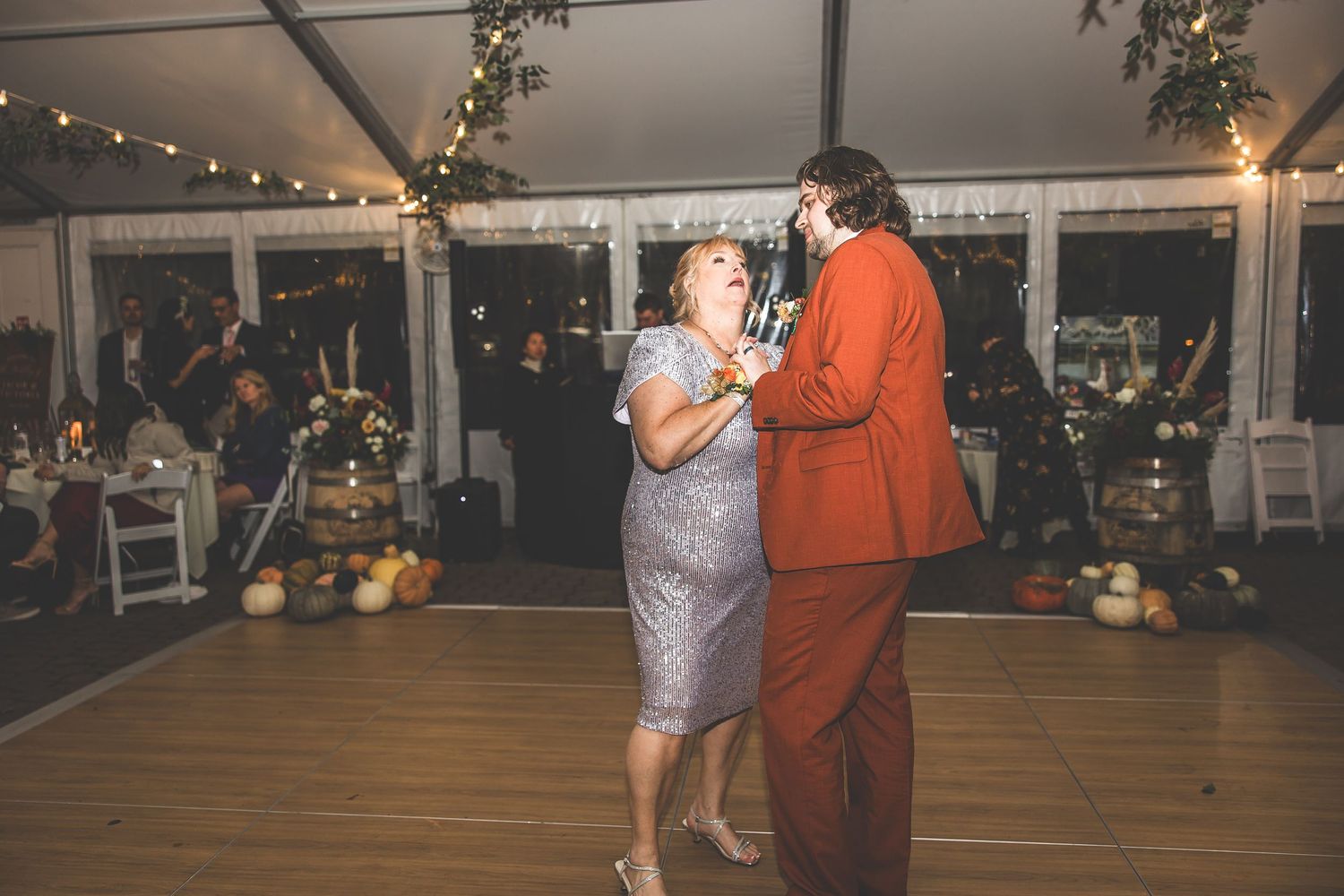 A couple dances together at a wedding reception under twinkling string lights and greenery decor.
