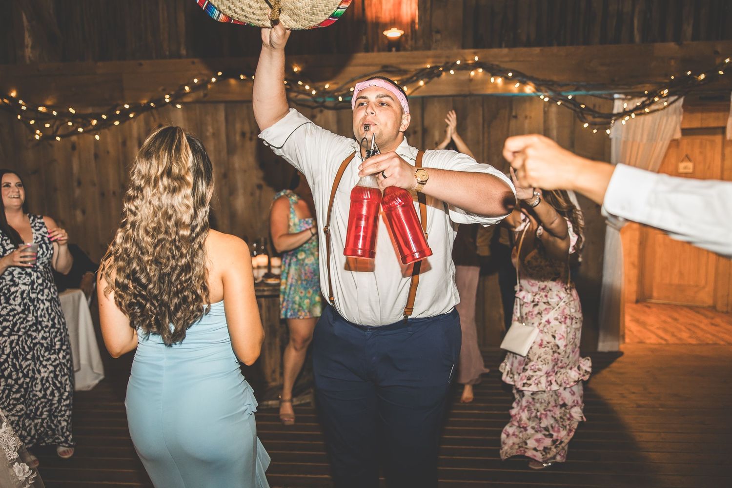 Wedding guests dancing and mingling under decorative string lights at an indoor reception.
