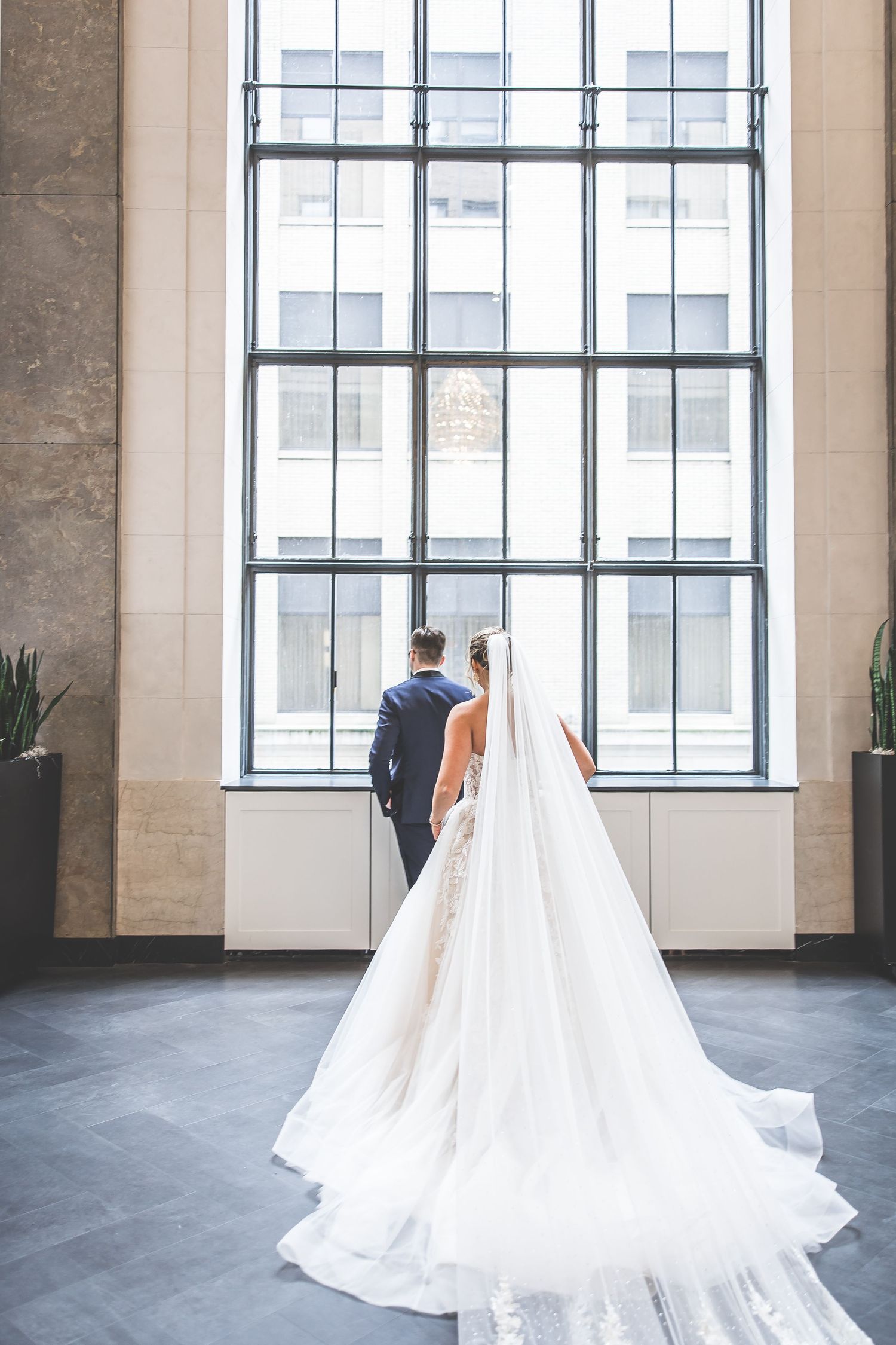 Elegant white wedding dress with flowing train photographed in front of large industrial windows.