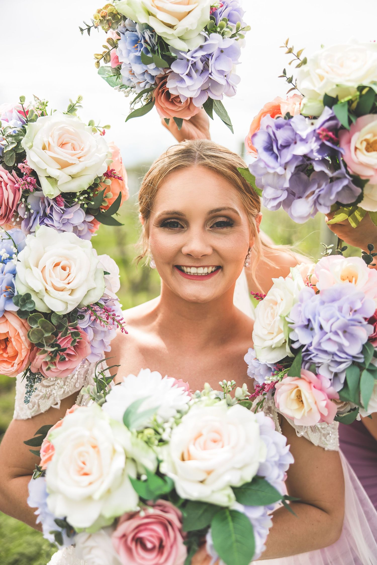 Wedding bouquets featuring purple hydrangeas, pink and white roses frame bridal portrait.