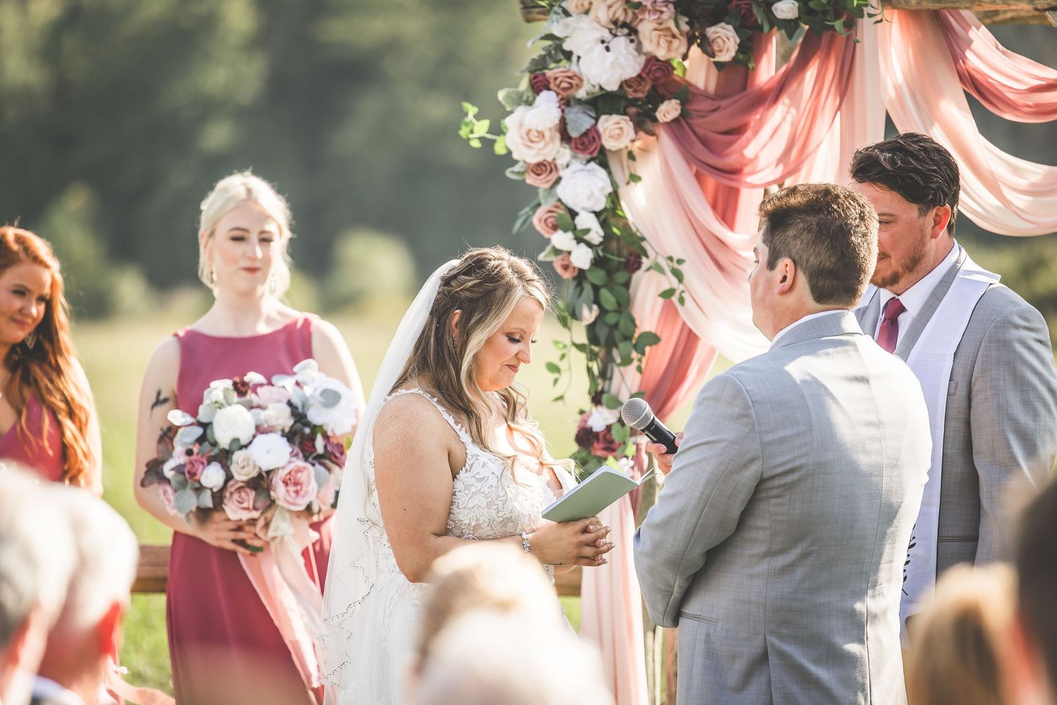 Close-up of wedding ceremony moment under pink draped arch with floral decorations.