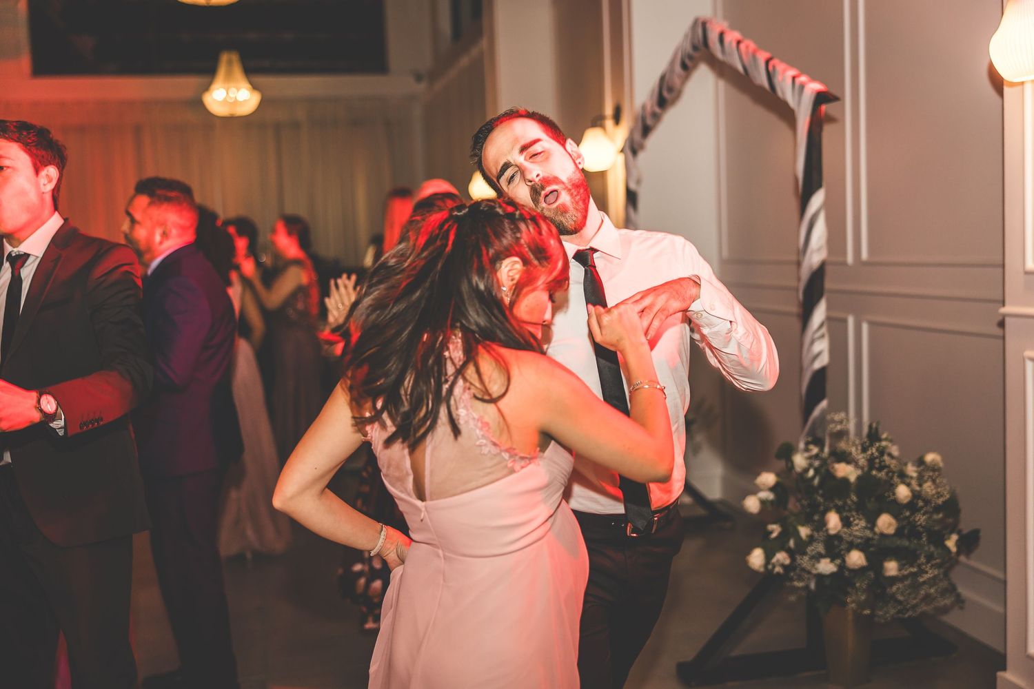 Wedding reception guests dancing energetically on the dance floor under warm lighting.