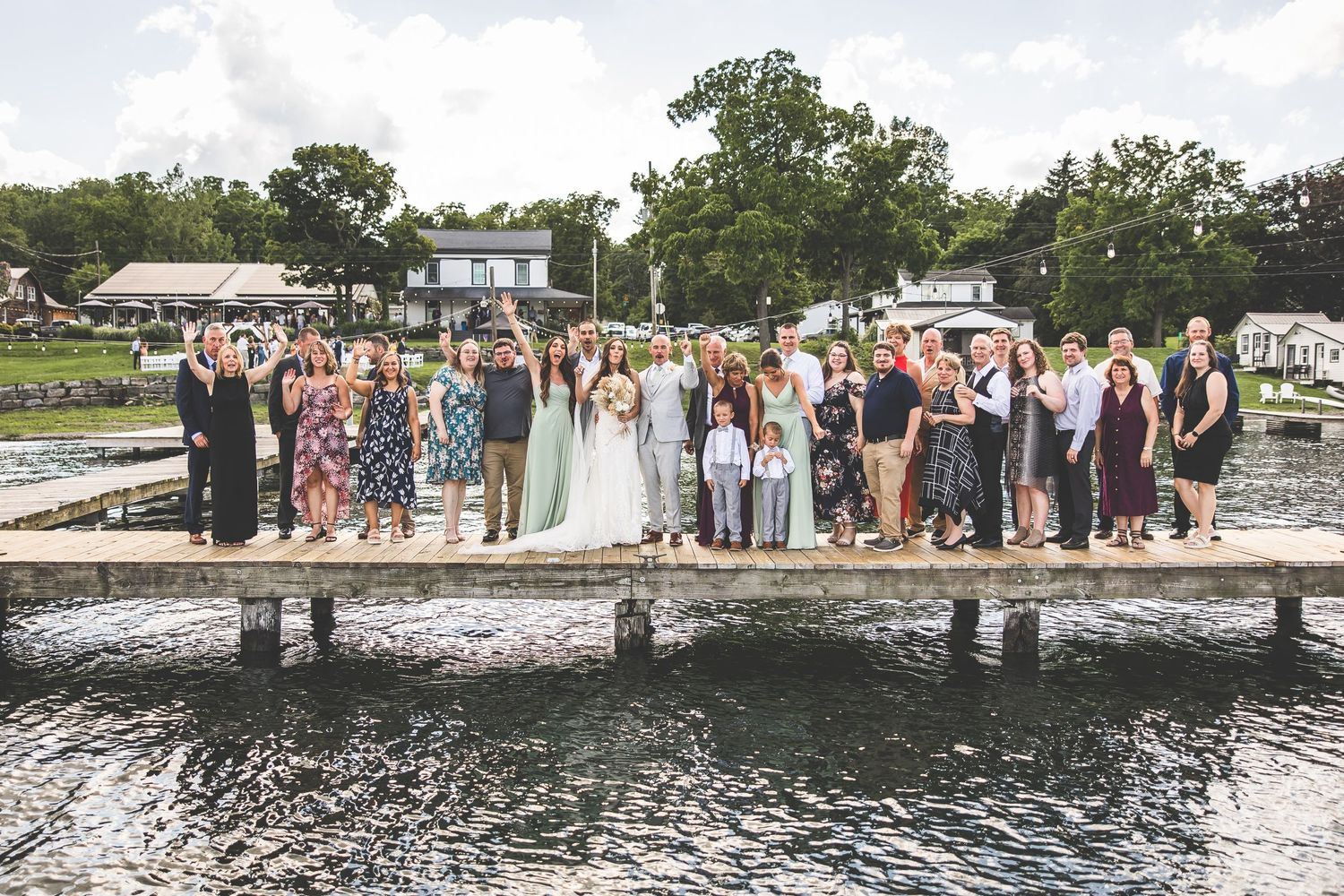 Wedding guests line up along a lakeside dock for a group photo.