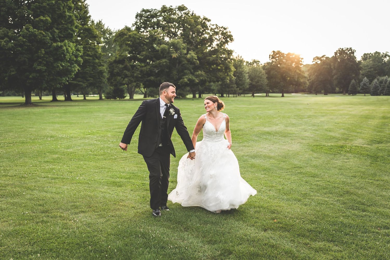 Newlyweds run joyfully across a green lawn during their wedding celebration.