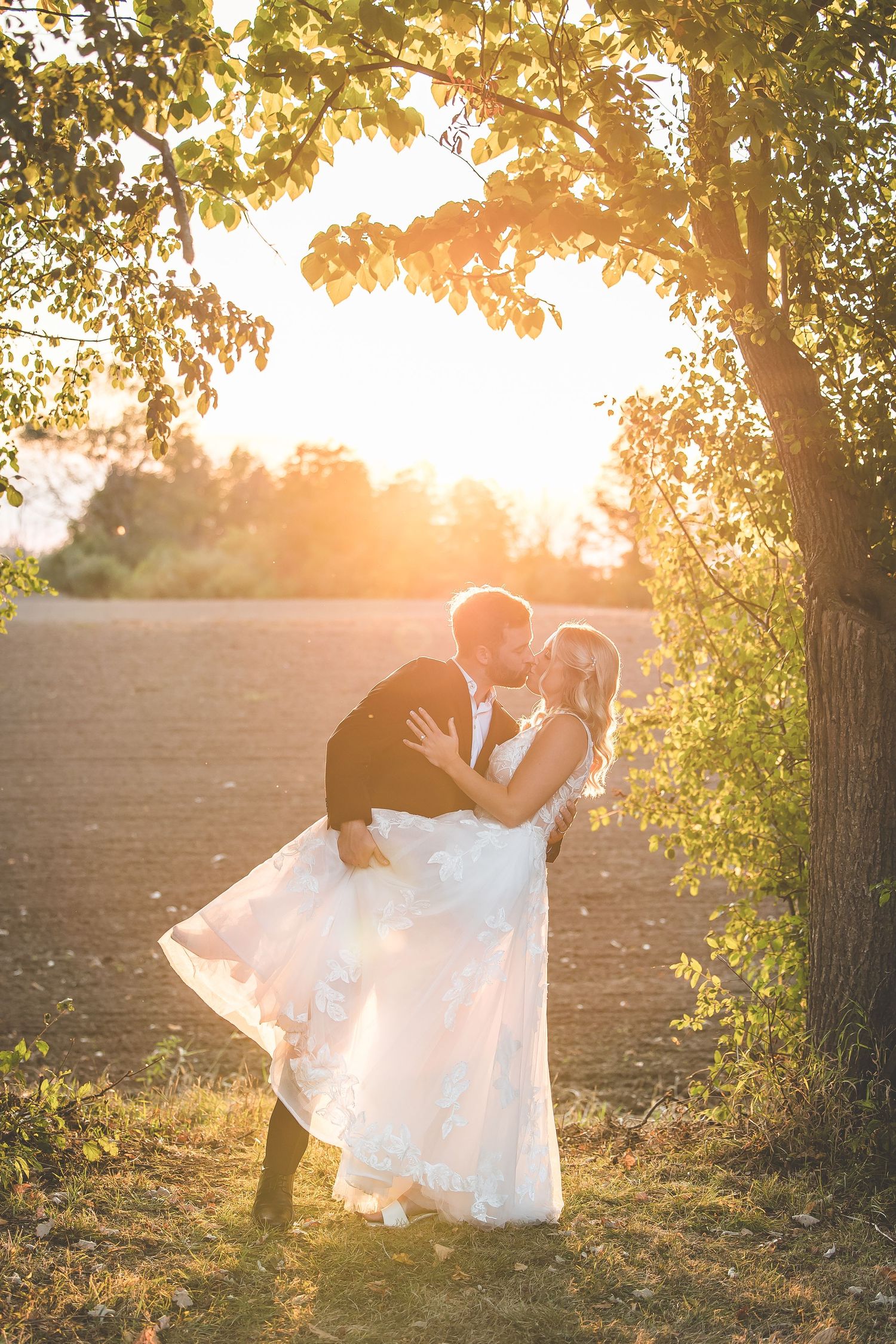 Romantic sunset wedding photos with couple silhouetted against golden light through trees.