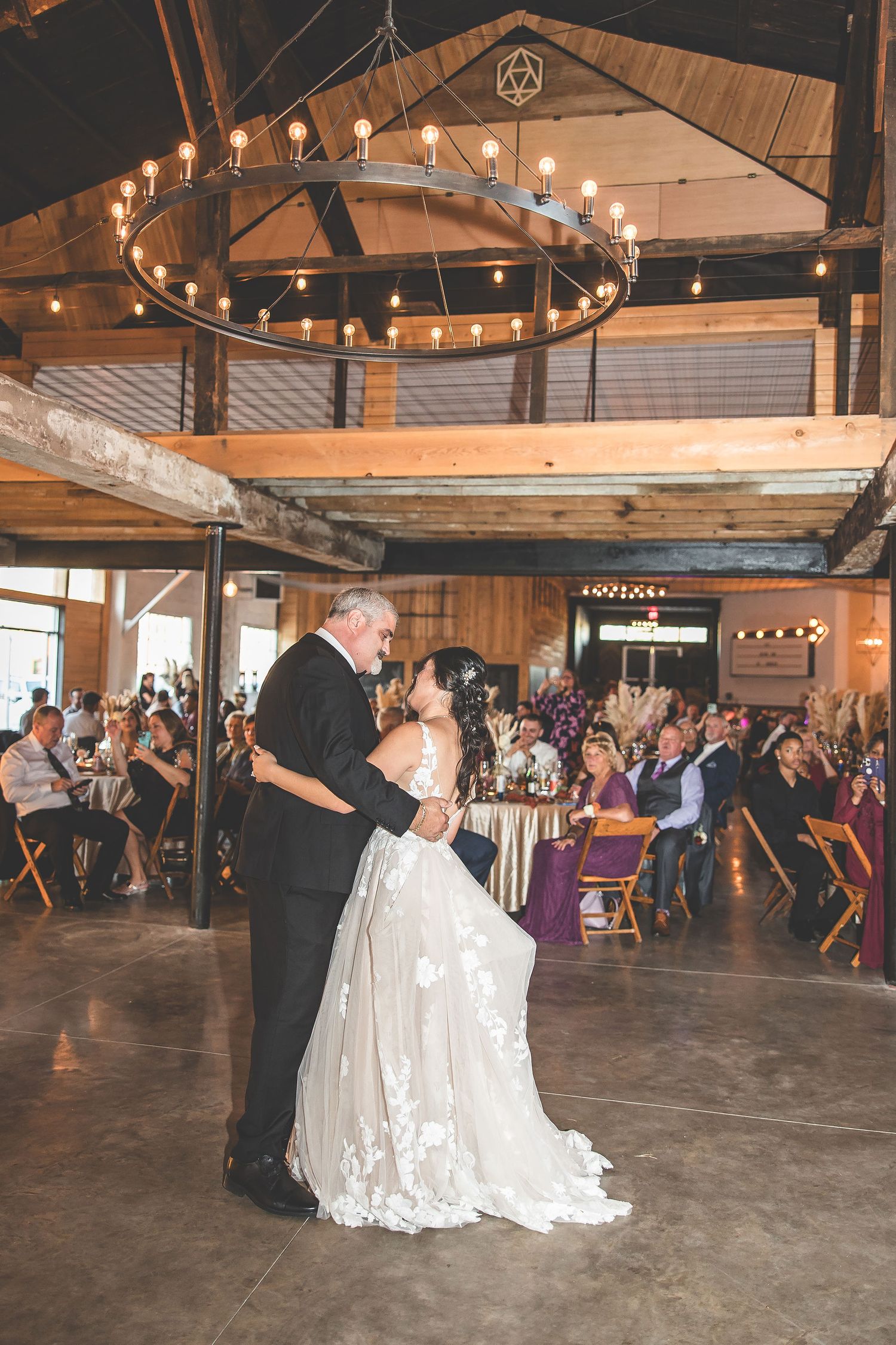 Wedding reception dance floor in rustic barn venue with exposed beams and string lights.