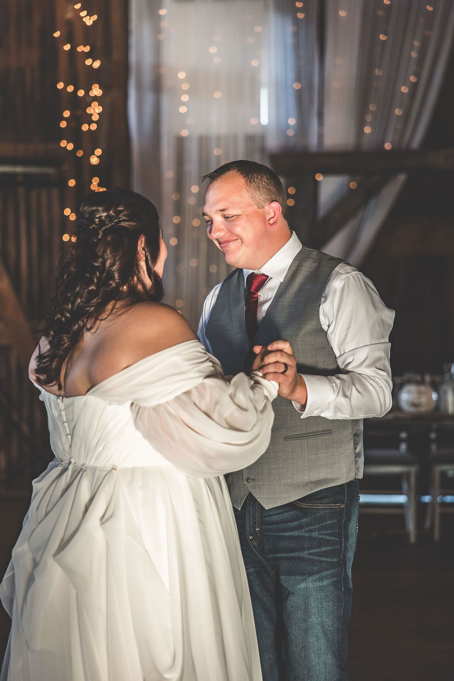 Dancing couples celebrate at a rustic barn wedding reception under warm lighting.