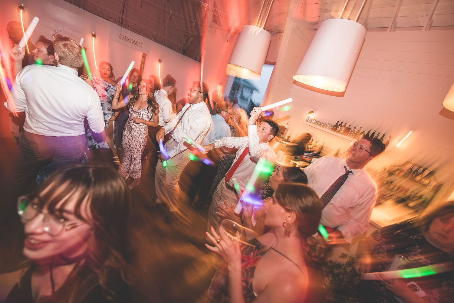 Wedding guests dancing energetically under pink lighting at a reception party.