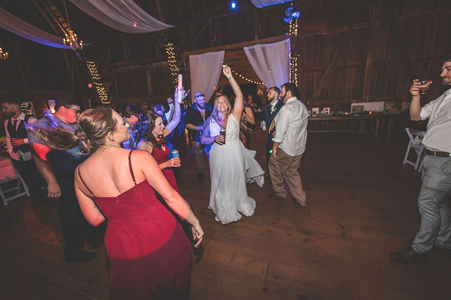 Wedding party dancing and having fun in a rustic barn setting with ambient lighting.