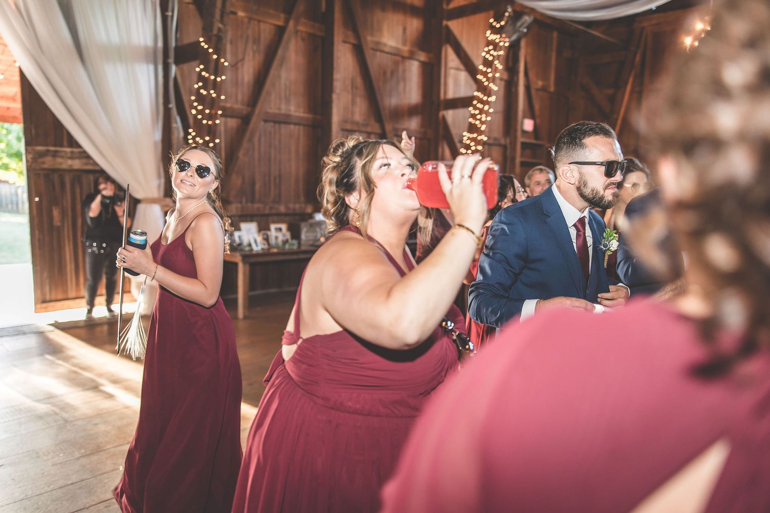Wedding guests enjoying themselves on dance floor at rustic barn reception with romantic lighting.