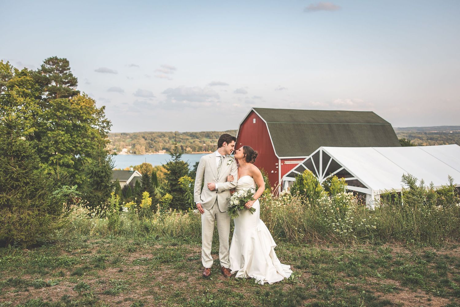 Scenic countryside wedding portraits with red barn and autumn landscape in background.