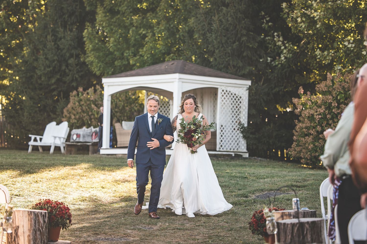 Outdoor wedding ceremony setup with white chairs and decorative arbor at sunset.