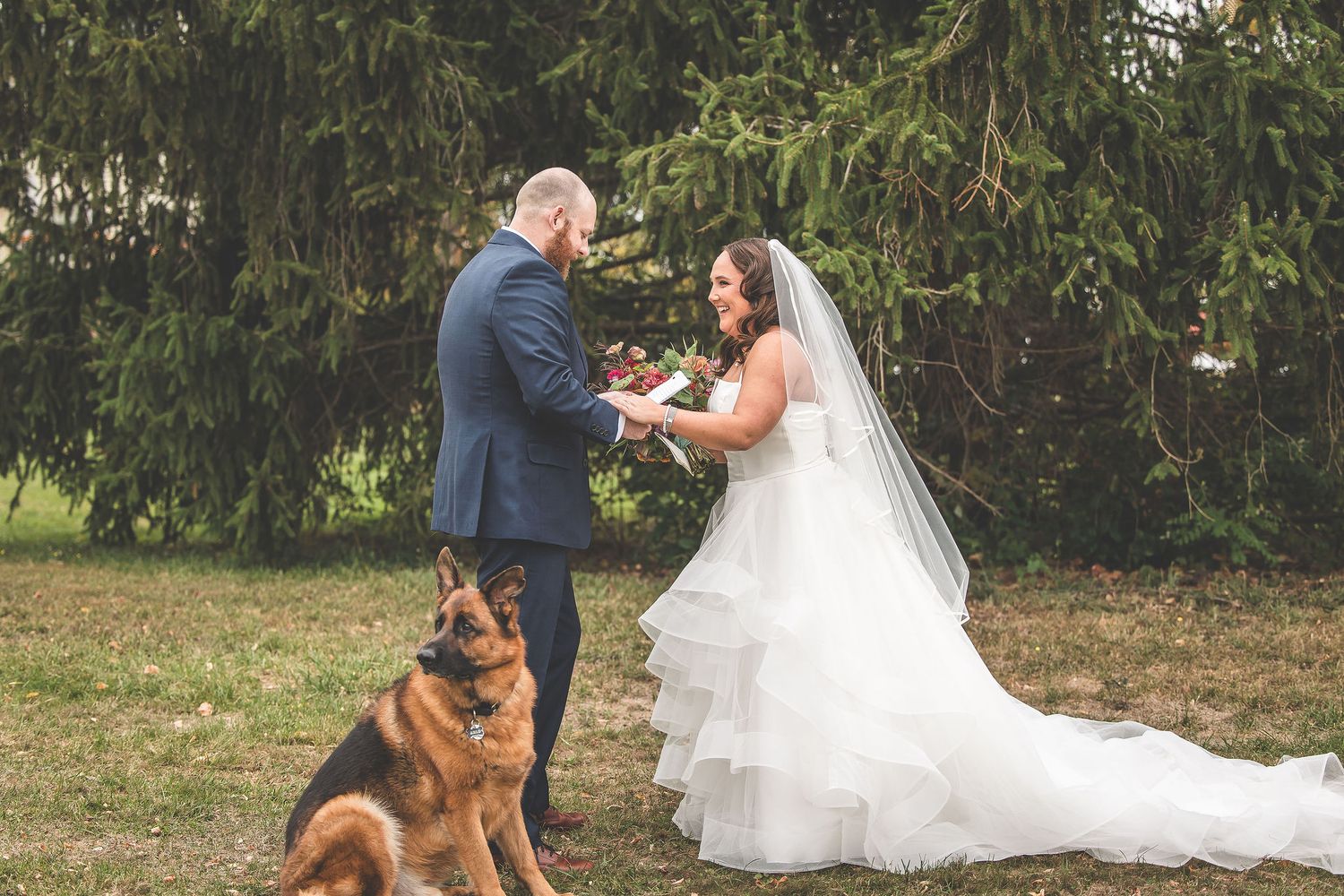 A couple exchanges rings during their outdoor ceremony with their loyal German Shepherd watching.
