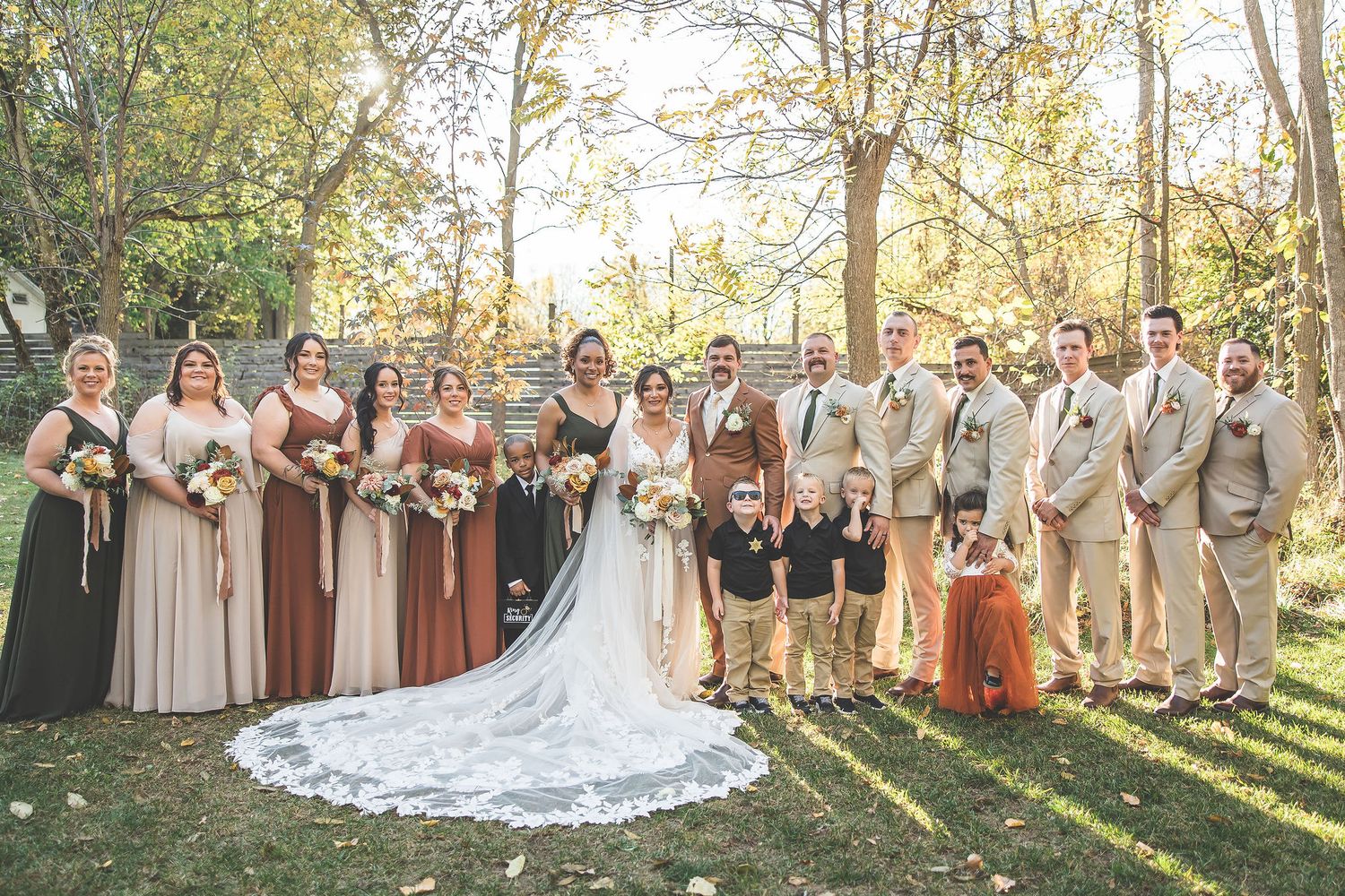 Wedding party poses for group photos in an outdoor setting with golden autumn light.