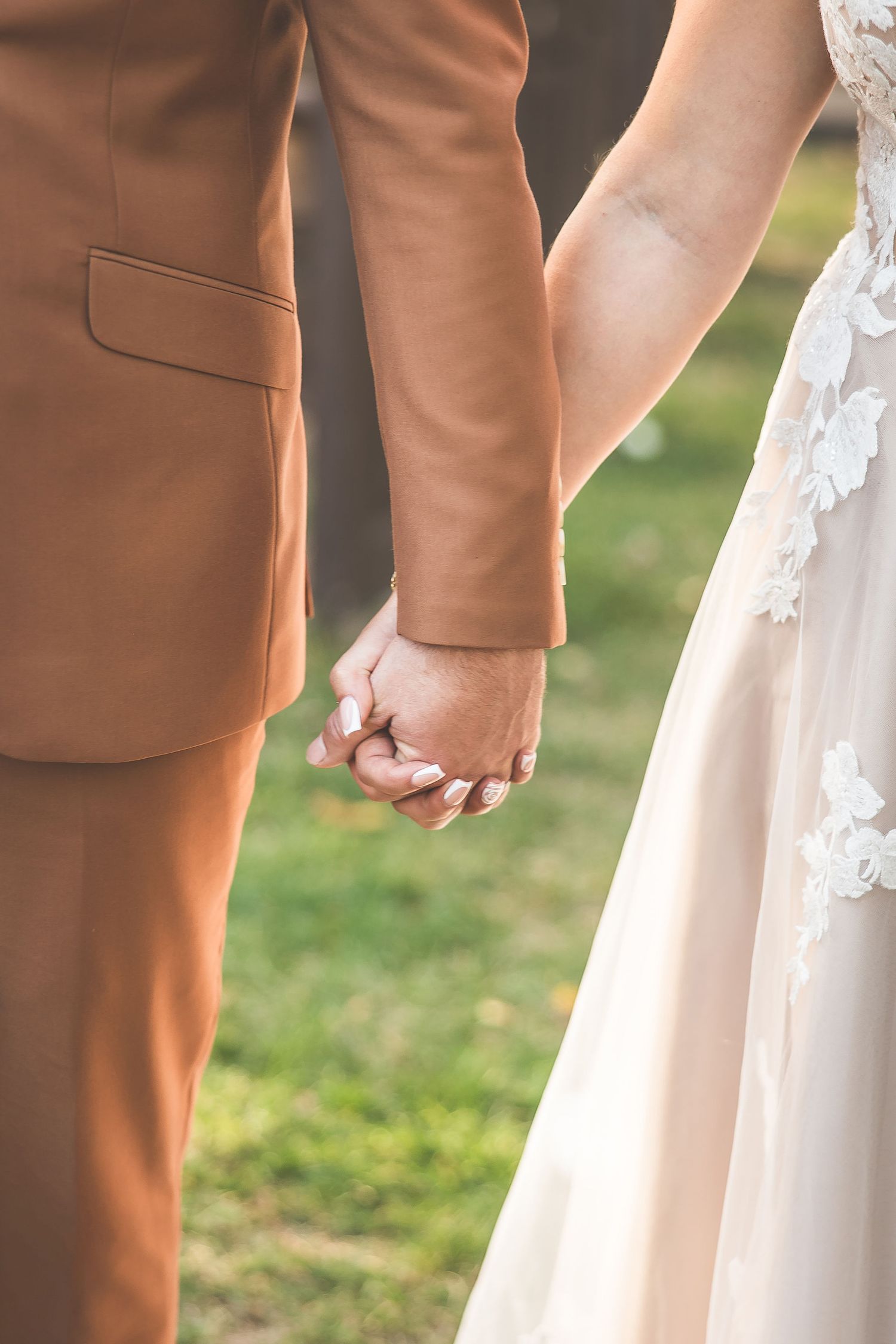 Close-up of wedding attire showing brown suit and white lace dress details.