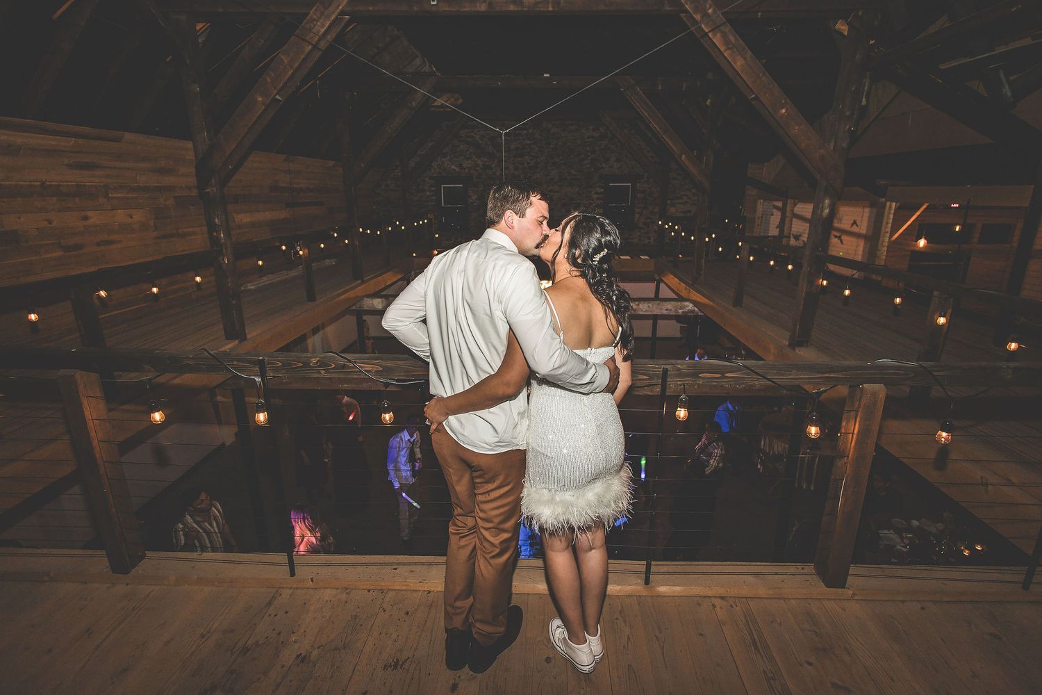 Couple shares an intimate moment on a rustic wooden balcony with string lights overhead.