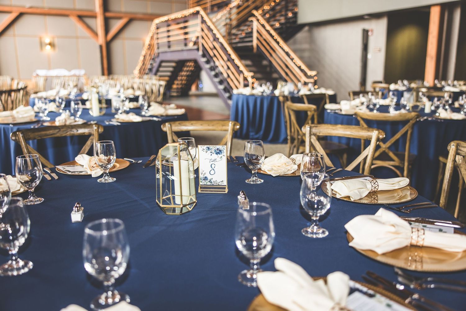 Wedding reception tables set with navy blue linens, wine glasses, and gold accents.