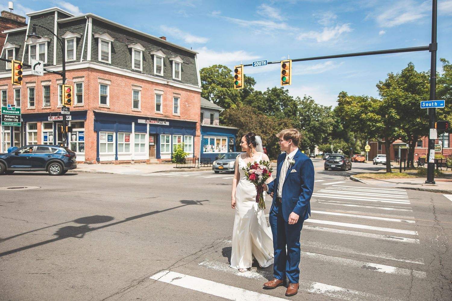 Urban wedding photo shoot at intersection with historic buildings and blue sky.