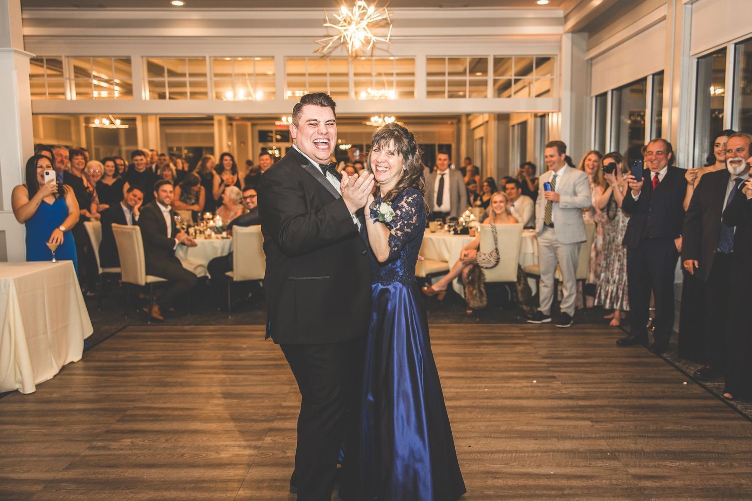 Formal couple dancing in an elegant ballroom with guests watching from tables in the background.