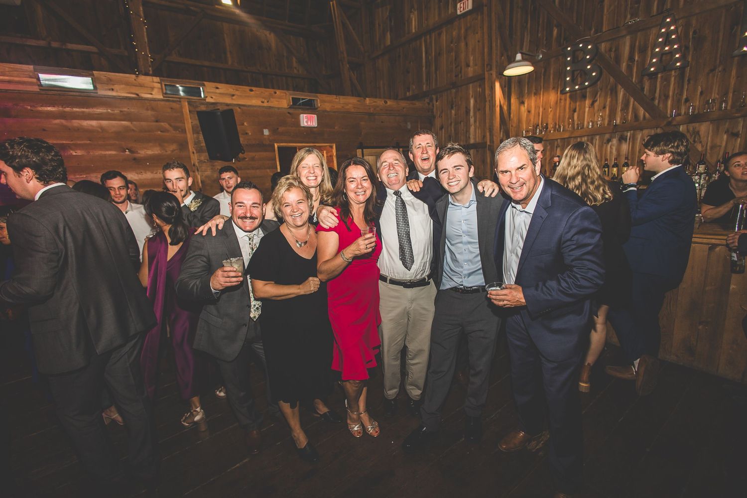 Wedding guests dance and celebrate on a rustic barn dance floor with wooden walls and festive lighting.