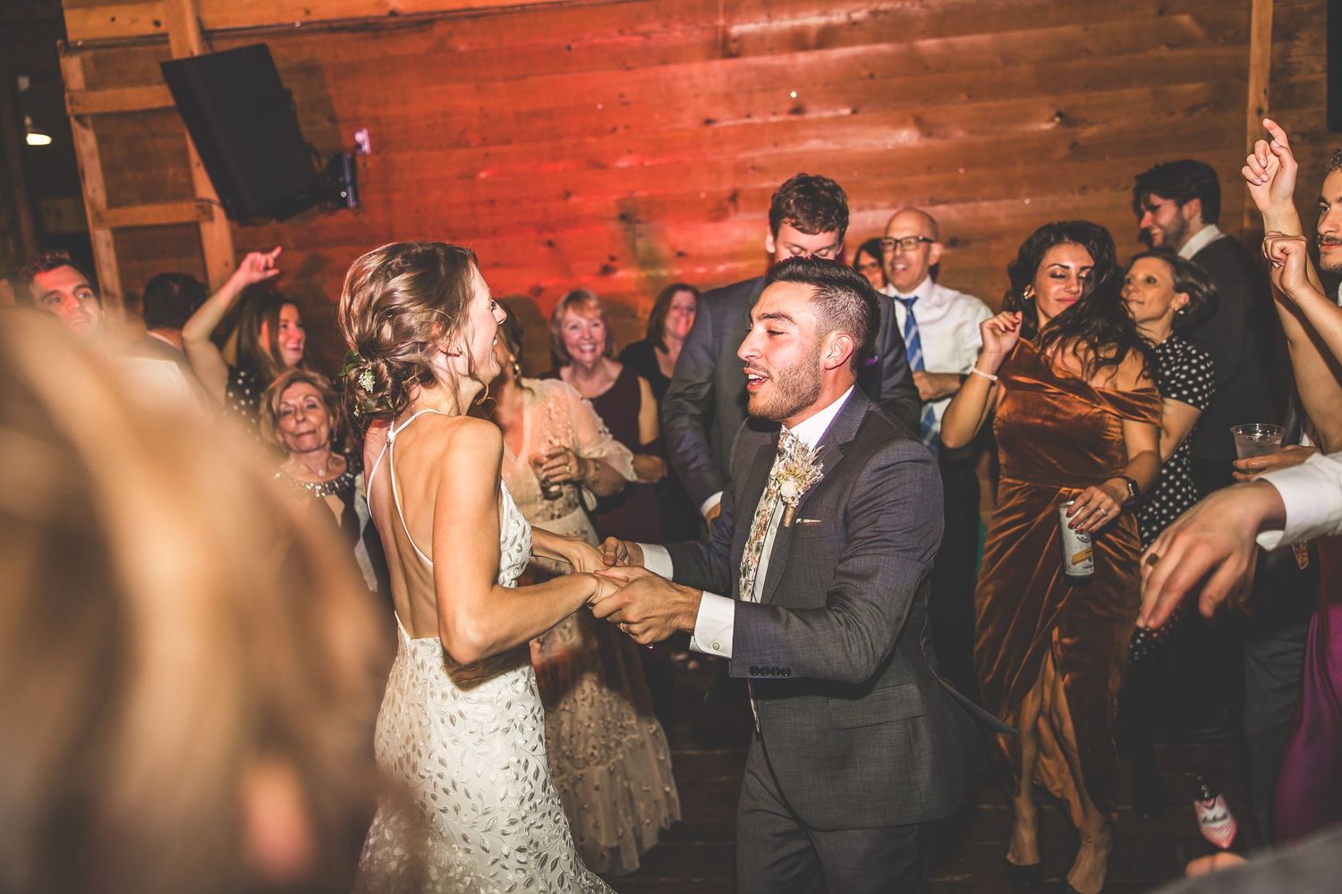 Energetic crowd dancing under red lighting at a wedding reception with wooden wall backdrop.