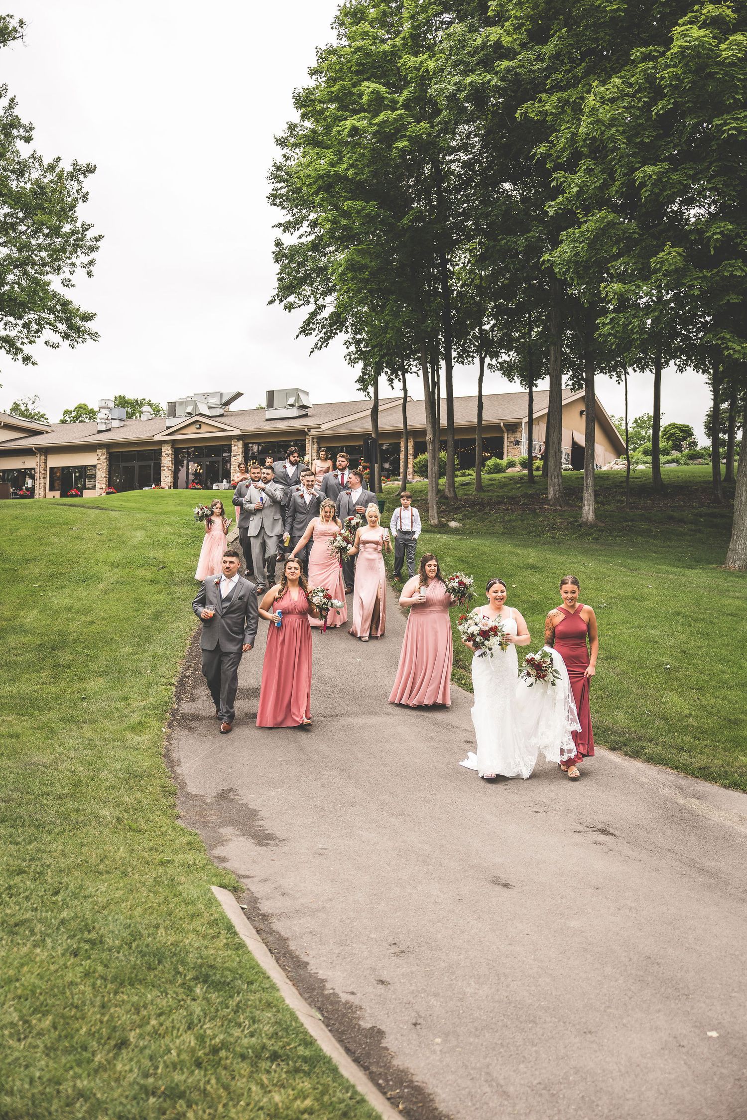 Wedding party in pink and coral dresses walks along outdoor pathway during celebration.