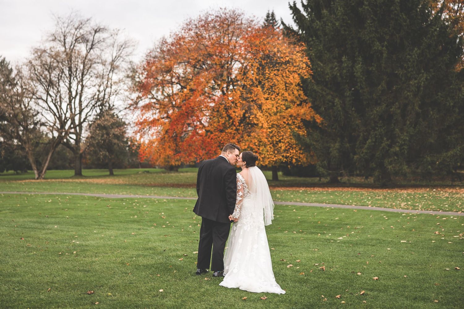 Wide landscape view of wedding couple in autumn garden setting.