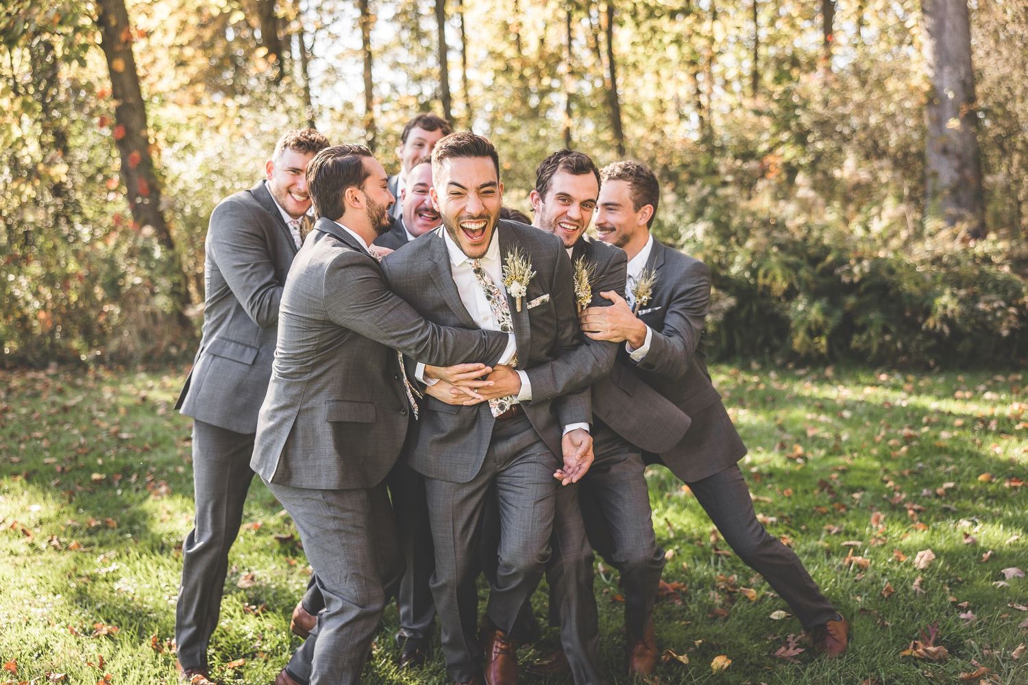 Groomsmen laughing and having fun together outdoors in gray suits.