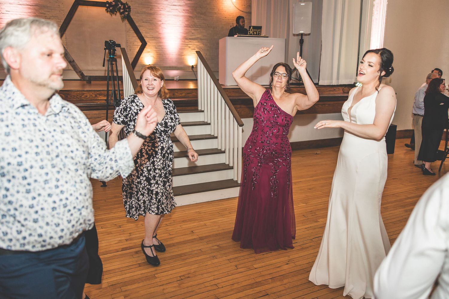 Wedding reception guests dancing and having fun in an elegant venue with white stairs.