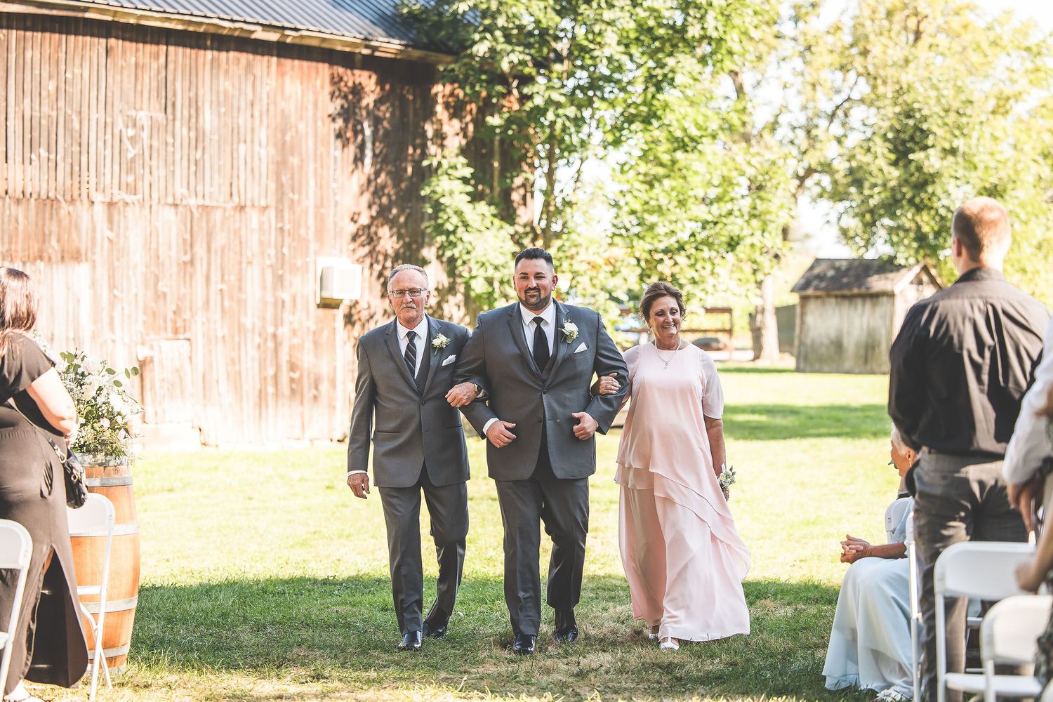Wedding party and guests gathered outside a rustic barn venue during a ceremony.