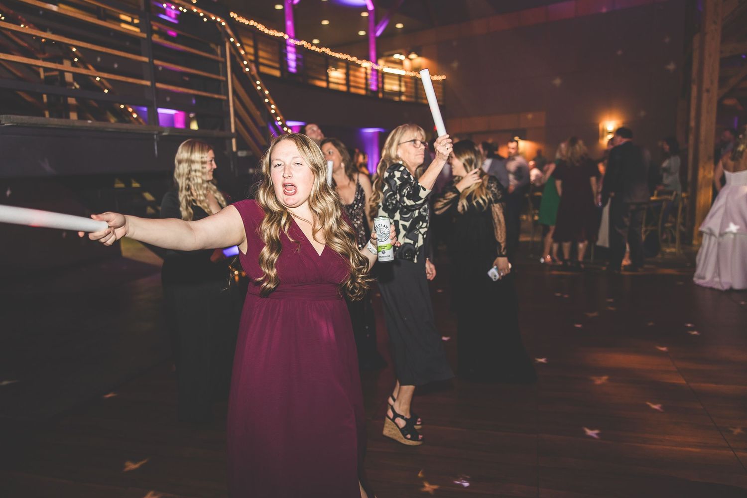 Wedding reception dance floor illuminated with purple lighting as guests celebrate.