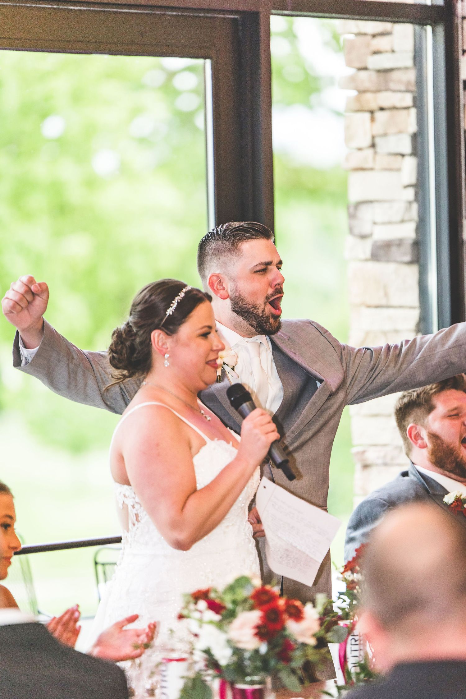Wedding party members laugh and celebrate during speeches at an elegant indoor reception.