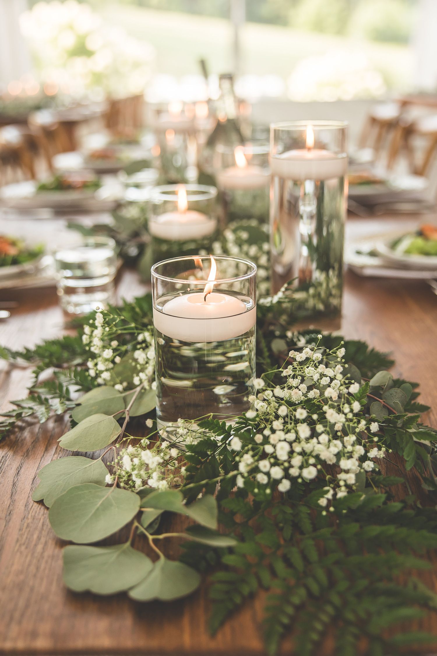 Romantic table centerpiece with floating candles surrounded by baby's breath and eucalyptus leaves.
