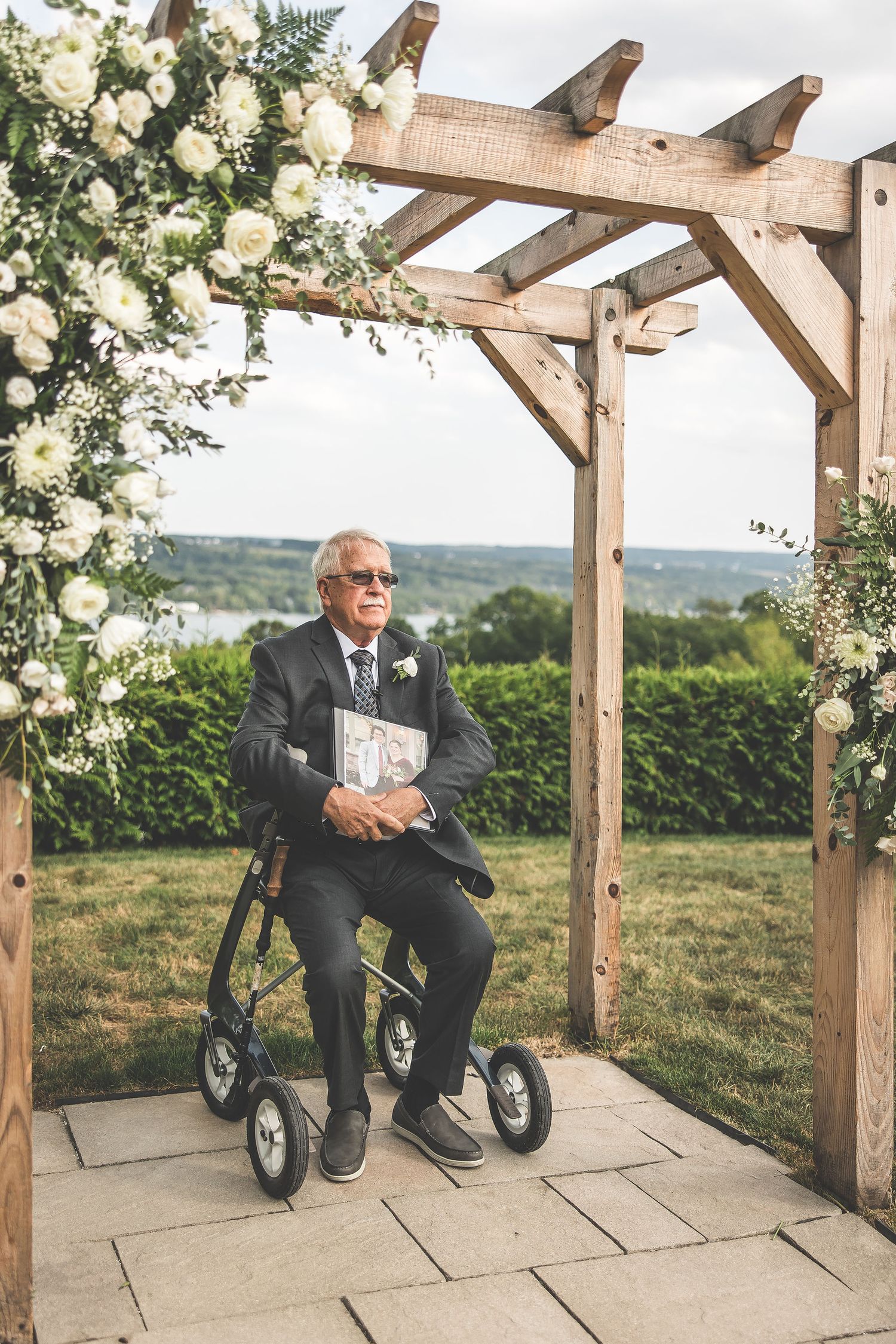 Wooden pergola decorated with white flowers and greenery against a scenic countryside backdrop.