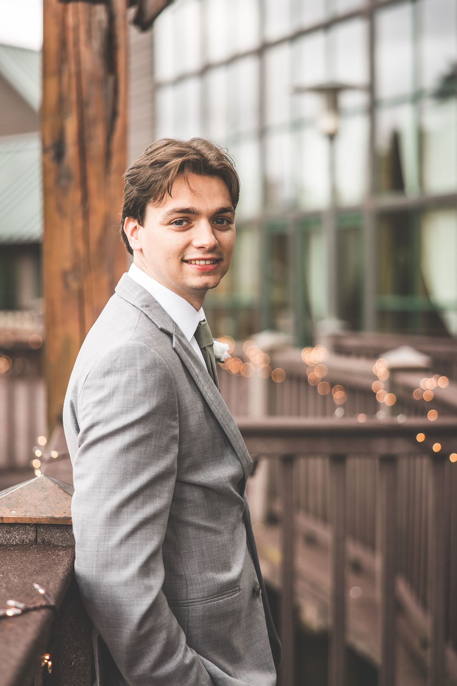 Portrait of groom in grey suit on deck with string lights.