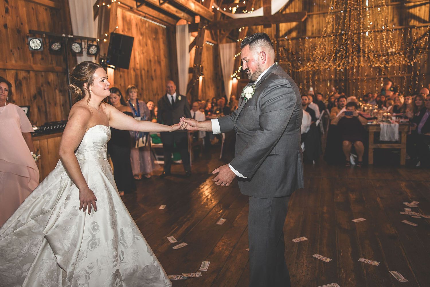 Elegant wedding reception dance in a rustic wooden barn with romantic lighting and guests watching.